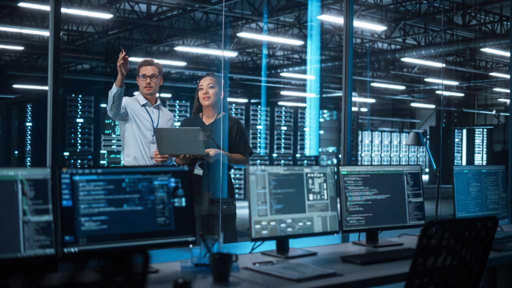 Successful Corporate Top CEO's Talking, Using Laptop Computer Standing in Big City Office at Night. Two Successful Managers Discuss Environmental, Social, Corporate Governance for e-Commerce Project