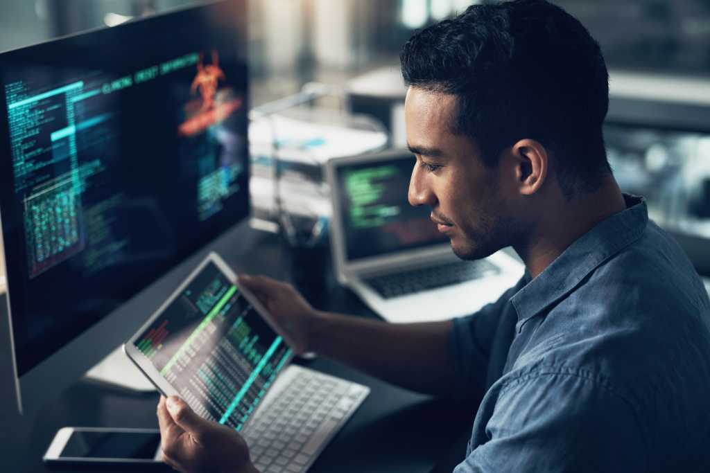 Shot of a young man using his digital tablet and computer in a modern office