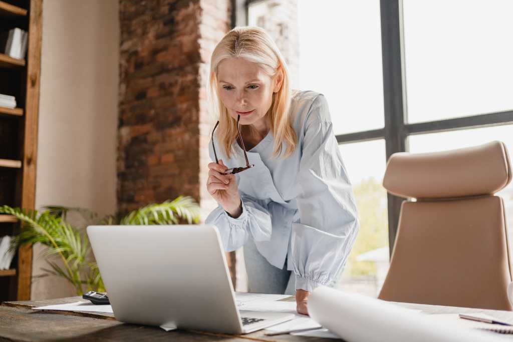 Concentrated businesswoman ceo at laptop, working at office desk with documents, searching surfing web internet online